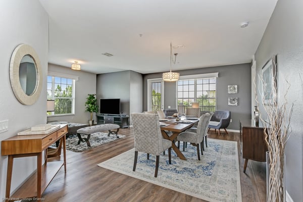 Open-plan living and dining area with gray walls, wood furniture, large windows, and pendant lighting