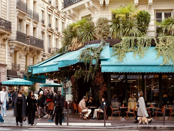 Parisian cafe with teal awning and outdoor seating surrounded by greenery