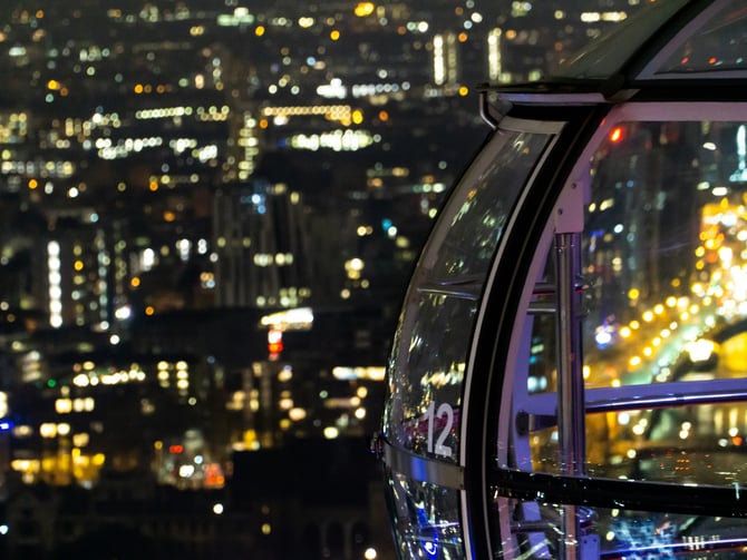 Illuminated ferris wheel gondola overlooking a city at night