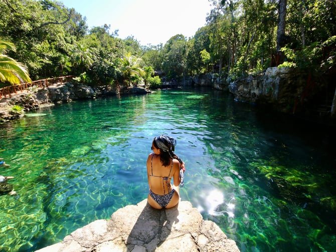 Woman sitting on a rock above a lush green cenote in the Yucatan jungle