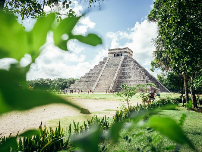 El Castillo pyramid at Chichen Itza framed by jungle leaves under a blue sky