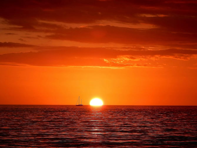 Deep orange Gulf sunset with a sailboat on the horizon