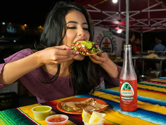 Woman eating a tostada at a street food stand at night
