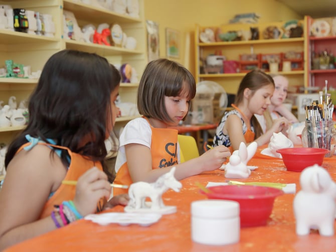 Children glazing clay figurines at an art studio table